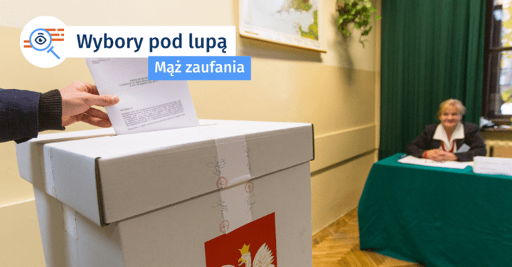 ręka wrzucająca kartę do urny wyborczej, a w tle członkini komisji wyborczej przy stole