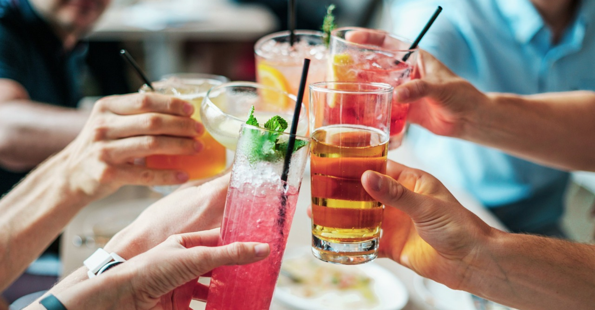 Osoby znajdujące się w restauracji/barze wznoszą toast, trzymając w rękach piwo lub drinka