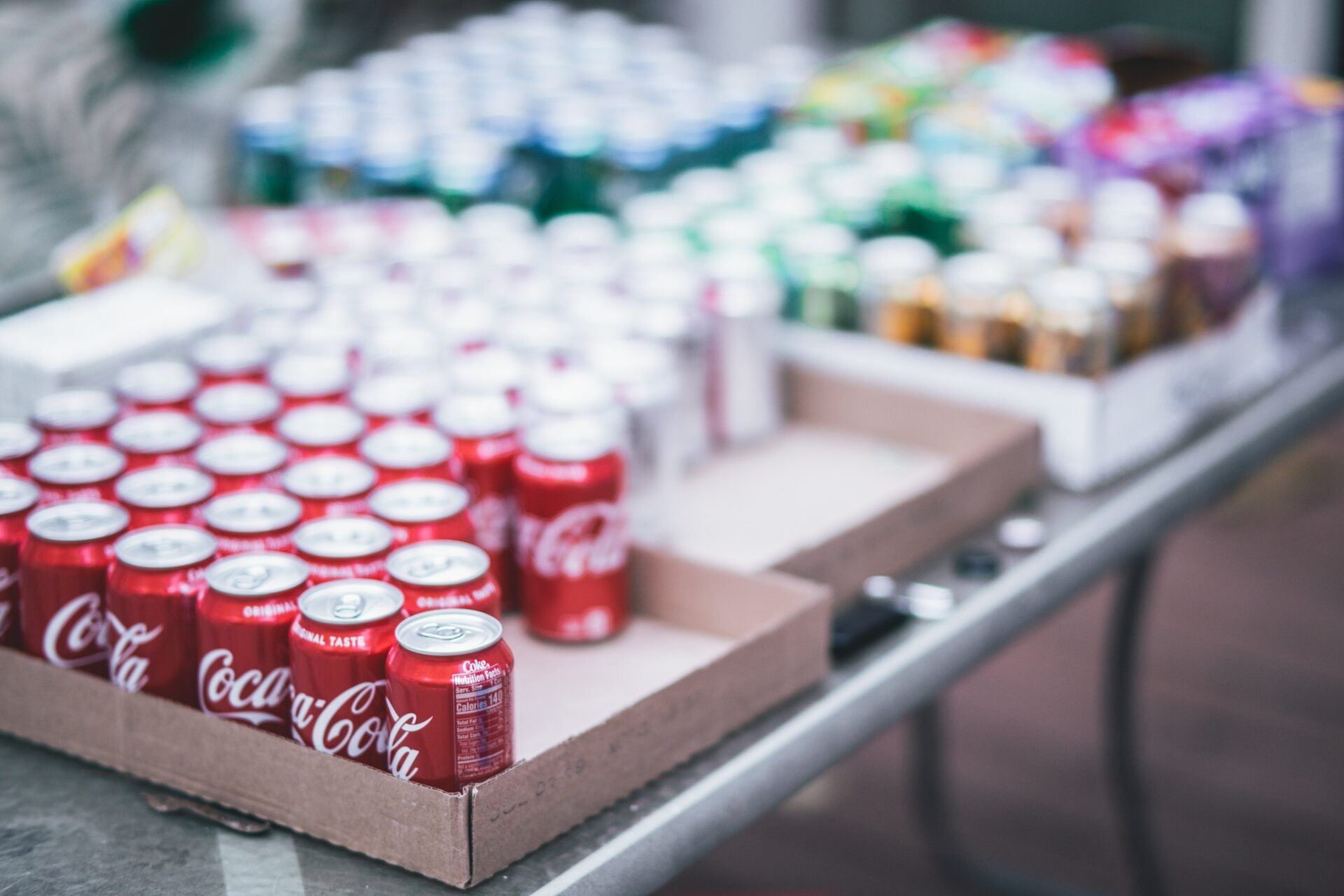 Papierowe skrzynki z napojami gazowanymi w puszkach, na pierwszym planie Coca-Cola.