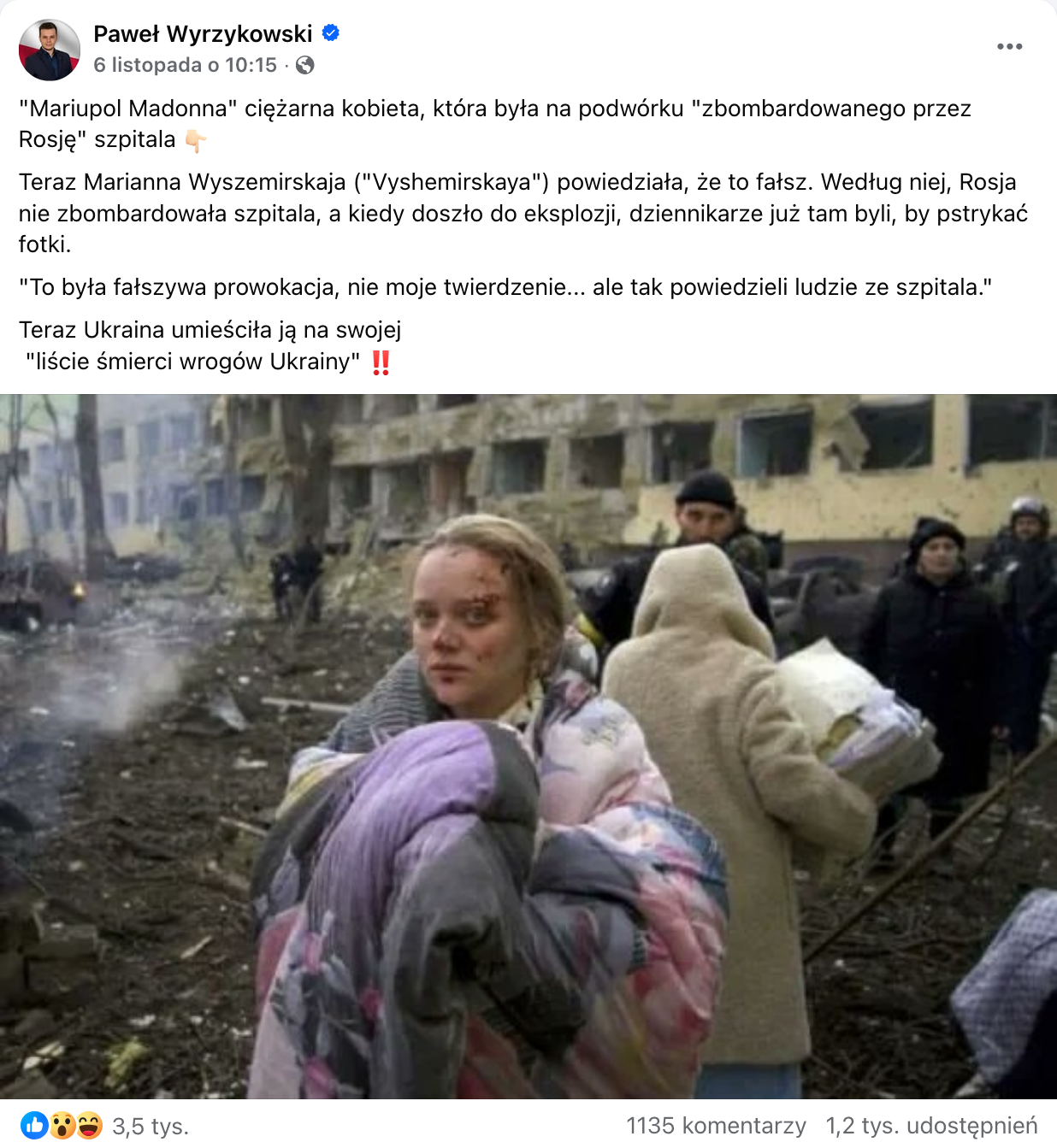 Zrzut ekranu przedstawiający wpis opublikowany na platformie Facebook.com. Do wpisu dołączono zdjęcie, na którym w pierwszym planie widać kobietę, a w tle zniszczony budynek, którego wszystkie okna nie mają szyb. Kobieta jest blondynką, spogląda prosto w aparat, ma zakrwawioną twarz, owinięta jest kolorową kołdrą. Za jej plecami widać kobietę w białym płaszczu, która coś niesie. Poza nimi na fotografii widocznych jest kilka osób ubranych na czarno.
