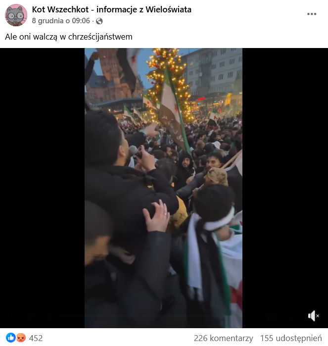 Zrzut ekranu wpisu z Facebooka. Na górze podpis i elementy interfejsu platformy, na dole klatka z nagrania, przedstawiająca grupę osób z flagami Syrii. W tle rozświetlona choinka.