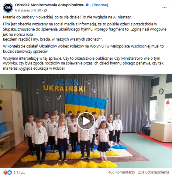 Wpis na Facebooku z nagraniem dzieci śpiewających ukraiński hymn. W kadrze widać grupę małoletnich stojących na środku sali, ubranych na czaro biało. W tle na kotarze zawieszono ukraińską flagę, a także zawieszono napis „dzień ukraiński”.
